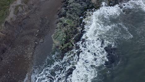 Aerial-top-down-view-of-waves-crashing-against-rocks,-Scarborough-coastline-UK