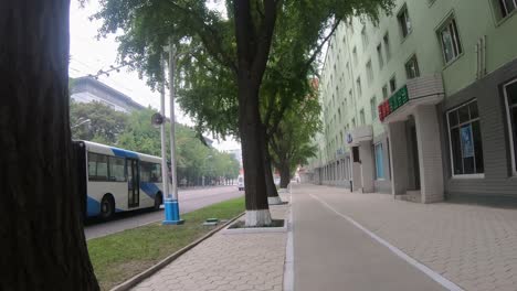First-person-POV-walking-along-footpath-of-Sungri-Street,-downtown-Pyongyang,-North-Korea