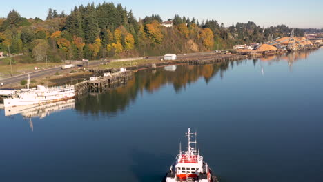 Slow-aerial-dolly-over-tugboat,-Coos-Bay,-and-sunny,-green-Oregon-coastline