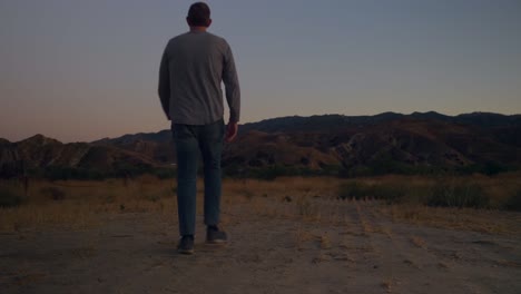 Static-shot-of-a-man-walking-into-frame,-on-the-Californian-countryside,-at-dusk,-sunny-evening-with-mountains-in-the-distance