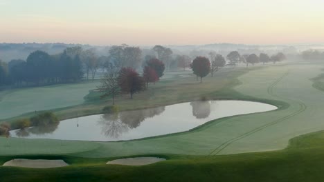 Aerial-above-water-hazard-on-misty-foggy-morning,-golf-course,-country-club-view,-beautiful-morning-light
