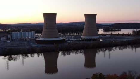 Aerial-industrial-scene,-cooling-towers-of-nucler-plant-with-riverfront-in-sunset,-atomic-power-generation,-dangerous-nuclear-energy,-environmental-risk-and-pollution-concept