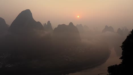 Aerial-shot-of-the-sun-shining-through-the-clouds-and-smog-in-an-isolated-mountain-range-in-Yangshuo,-China