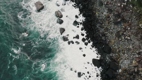Tilt-Up-Aerial-View-of-Sea-Waves-Breaking-on-Coast-Under-Breathtaking-Rocky-Cliffs-of-Isle-of-Skye-Island,-Scotland-UK