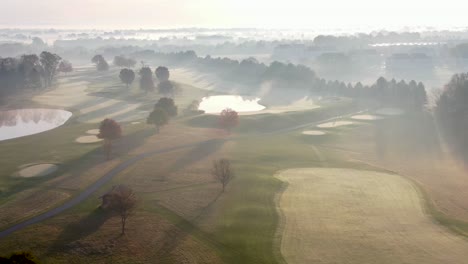 Cinematic-aerial-of-sunrise-burning-off-fog-above-gorgeous-country-club-golf-course,-autumn-leaves