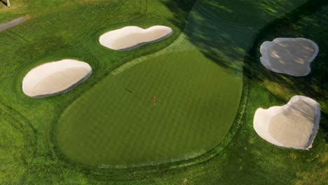 Aerial-tilt-down-of-golf-course-green,-sand-traps-during-beautiful-morning-light
