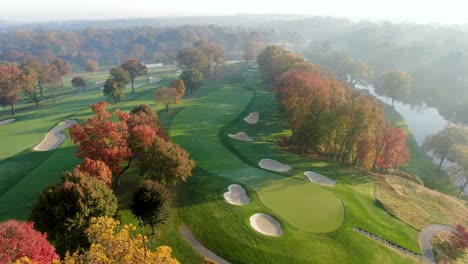 Slow-tracking-shot-above-golf-course-green,-sand-trap-hazards,-fall-leaves-and-river