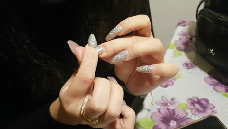 Brunette-woman-is-looking-on-her-fresh-made-sparkling-nails-after-her-manicure