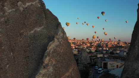 Reveal-shot-from-behind-the-rocks-of-hot-air-balloons-over-Goreme-Cappadoica,-Turkey