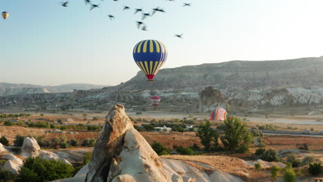 Trucking-shot-of-hot-air-balloon-at-Goreme-Cappadocia-with-starlings-flying-in-the-foreground