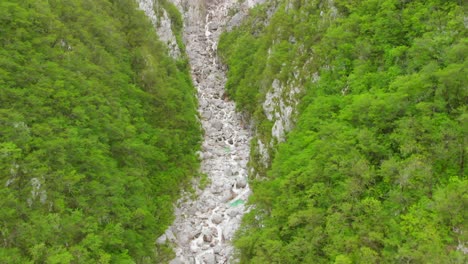 Aerial-footage-of-a-waterfall-and-river-going-through-a-green-and-steep-canyon-in-Slovenia