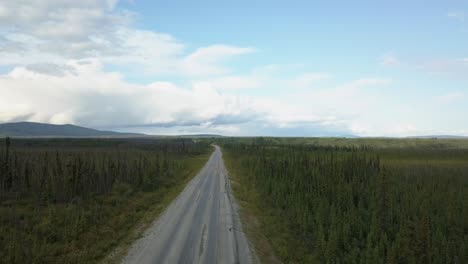 Drone-shot,-truck-driving-on-a-country-road,-spruce-forest-in-the-background-along-the-Alaskan-Highway