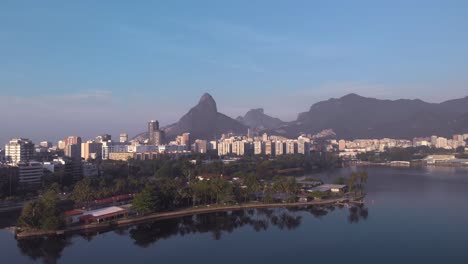 Aerial-tilt-up-showing-the-city-lake-island-and-club-Caiçaras-in-Ipanema-in-the-foreground-reveailing-Leblon-and-Two-Brothers-mountain-in-the-background-at-early-morning-sunrise