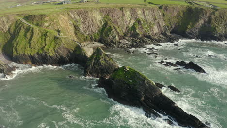 Aerial-view,-Dunquin-Pier-is-situated-in-a-small-secluded-bay-surrounded-by-rocky-cliffs,-famous-postcard-image-of-Ireland,-surrounding-landscape-is-an-attractive-mixture-of-mountain-and-cliff-top