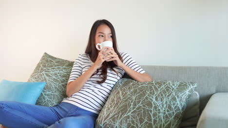 Pretty-Asian-girl-smiling-as-she-enjoys-her-morning-cup-of-coffee