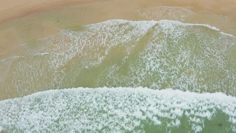 Aerial-shot-of-ocean-waves-crashing-against-an-beautiful-beach