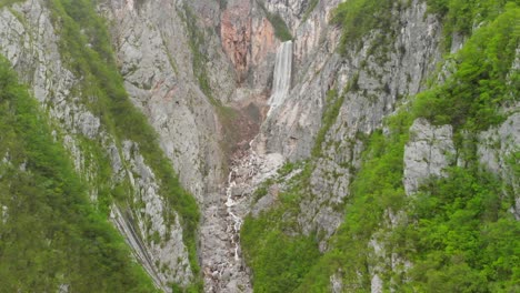 Aerial-footage-of-a-waterfall-and-river-going-through-a-green-and-steep-canyon-in-Slovenia