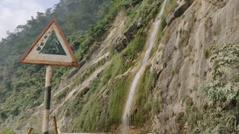 Street-sign-showing-landslide-area-and-beautiful-waterfall-fall-down-from-the-mountains-in-the-backdrop