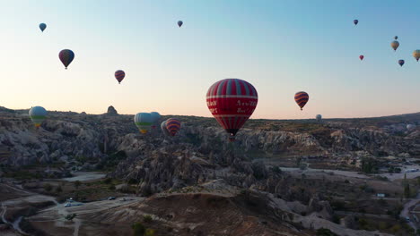 A-flotilla-of-hot-air-balloons-flying-above-the-Jurassic-landscapes-of-Goreme-Cappadoica,-Turkey