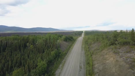 Fast-moving-aerial-shot-of-rough-roads-in-the-countryside,-mountain-range-and-grass-in-the-background-on-Alaskan-highway