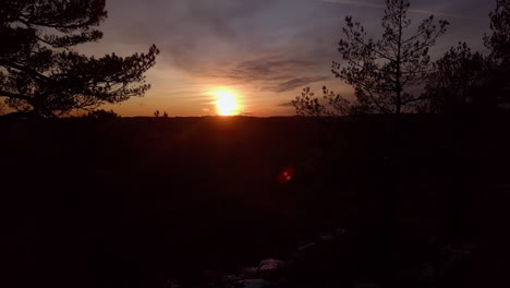 Aerial,-rising,-drone-shot,-behind-forest,-looking-at-the-sunset,-at-the-Dyblemyrheia-hill,-on-sunny,-autumn-day,-in-Lillesand,-Aust-Agder,-South-Norway