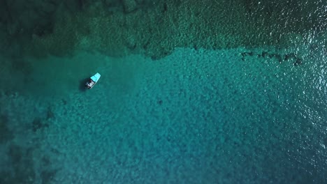 Static-aerial-view-of-a-boat-floating-on-crystal-clear-water-above-a-tropical-coral-reef