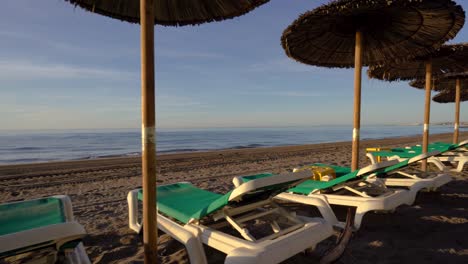 Interesting-gimbal-stabilized-shot-of-Marbella-beach-with-sunbeds-and-parasols,-dynamic-4k-smooth-moving-footage-of-costa-del-sol-coastline-at-sunrise