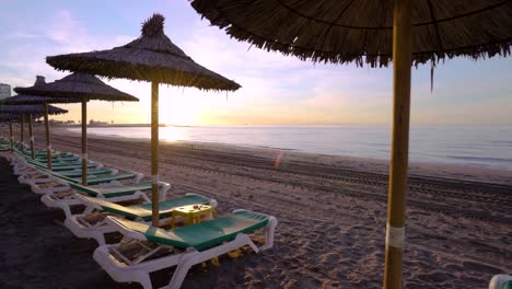 Sich-Stetig-Bewegender-Sonnenaufgang-Marbella-Strand-Mit-Sonnenschirmen,-Traumurlaubsziel,-Kardanische-Glatte-4k-aufnahme
