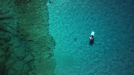Rising-aerial-view-of-a-boat-floating-above-a-coral-reef-above-crystal-clear-water