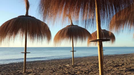 Gimbal-shot-of-parasols-on-marbella-beach-at-sunrise,-holiday-vacation-dynamic-footage