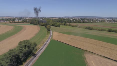 Luftaufnahme-Der-Amischen-Landschaft-Des-Landwirtschaftlichen-Arbeitsfeldes-An-Einer-Eisenbahnstrecke,-Während-Sich-Eine-Dampfmaschine-Nähert,-Wie-Sie-Von-Einer-Drohne-Gesehen-Wird