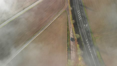 A-road-through-a-rural-agricultural-area-in-Luxembourg,-top-down-shot-of-a-morning-with-fog