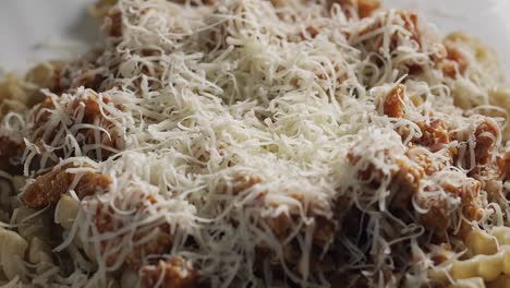 Close-up-of-sprinkling-shredded-cheese-on-pasta-bolognese,-static-shot