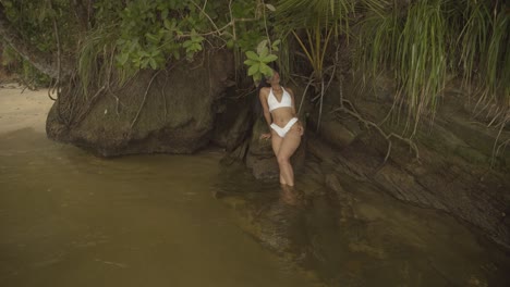 A-model-sitting-in-a-river-wearing-a-micro-bikini-and-posing-for-the-video-shoot