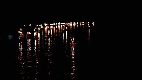 Krathong-Schwimmt-Im-Dunkeln-Auf-Einem-Strom,-Während-Er-Sich-Während-Loi-Krathong-In-Thailand-Auf-Weitere-Schwimmende-Kerzenlichter-Zubewegt,-Die-Sich-Am-Anderen-Ende-Des-Stroms-Versammeln