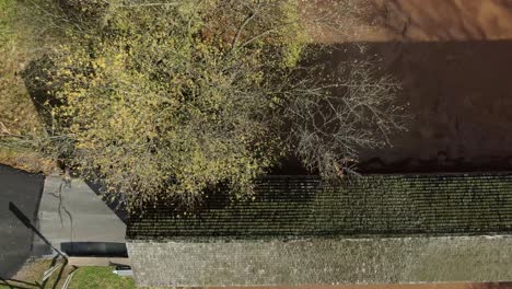 White-SUV-drives-up-to-and-through-covered-bridge-over-muddy-river-water,-aerial-drone-view