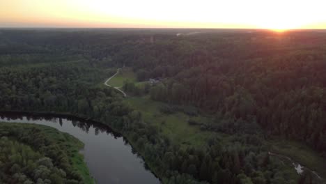 Aerial-view-of-river-between-forests-with-medieval-fortress-in-distance---flying-towards-sunset