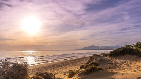 Long-time-lapse-of-sun-setting-over-Marbella-beach-with-people-walking-along-the-coast-line-with-a-beautiful-sunset,-spanish-vacation-in-the-coast-del-sol,-malaga,-spain