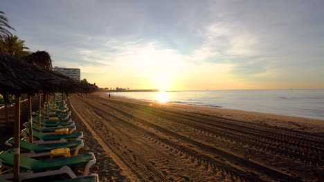 Gimbal-shot-moving-past-straw-beach-umbrella-to-reveal-beautiful-sunrise-on-marbella-beach