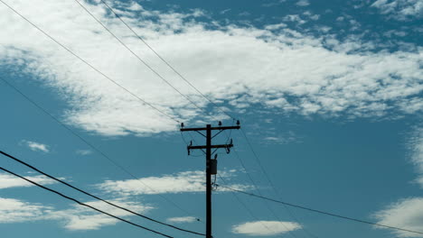 Zeitraffer,-Weiße-Wolken-Ziehen-An-Strommasten-Und-Drähten-Im-Blauen-Himmel-Vorbei