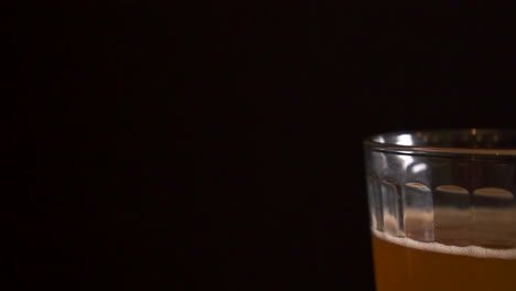Half-drunk-pint-of-beer-sitting-on-a-bar-table-with-a-black-background,-slow-motion-truck-right