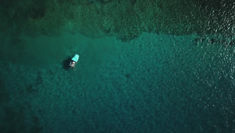 Rising-aerial-view-of-a-boat-relaxing-above-a-coral-reef-found-in-crystal-clear-water