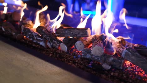 Camera-truck-left-slowly-of-fire-flames-in-a-modern-fireplace,-indoor-at-night-with-purple-lighting-background,-close-up-in-slow-motion