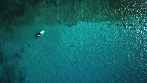 Aerial-view-above-a-boat-anchored-above-a-coral-reef-found-in-crystal-clear-water