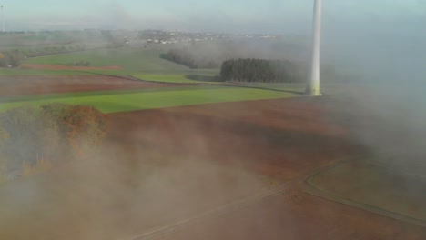 Revealing-aerial-shot-of-a-rural-area-in-Luxembourg-showing-a-windturbine,-during-a-morning-with-fog