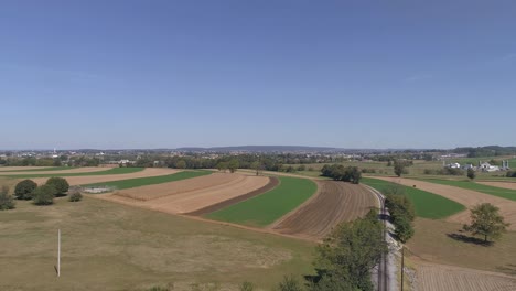 Aerial-View-of-Amish-Countryside-of-Farmer-Working-Field-by-a-Rail-Road-Track-as-a-Steam-Engine-Approaches-as-Seen-by-a-Drone
