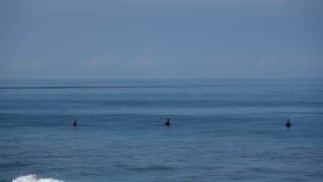 Drei-Surfer-In-Der-Ferne-Warten-Auf-Wellen,-Die-Auf-Brettern-Im-Meerwasser-Sitzen