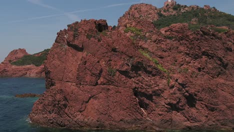 Seabird-Takes-Off-Fly,-Red-Craggy-Rock-Headland,-Coast,-CIRCLE-AERIAL