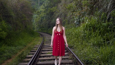 Young-girl-in-red-dress-walking-along-the-railway-tracks