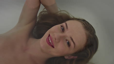Smiling-woman-in-bathtub-taking-bath-and-looking-to-camera